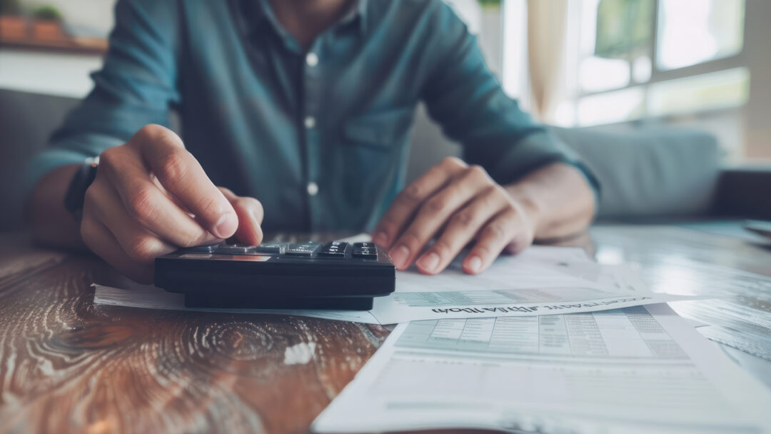 Person using a calculator while reviewing bills and financial documents at home