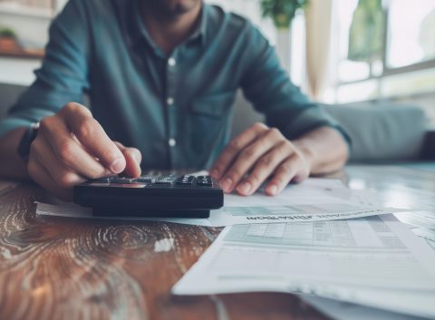 Person using a calculator while reviewing bills and financial documents at home