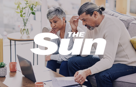 Older couple sitting on a couch reviewing documents and a laptop, with The Sun logo overlayed.