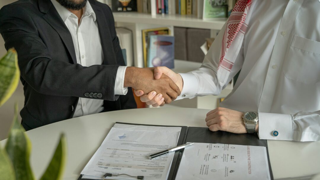 Two men shaking hands over a signed agreement at a desk